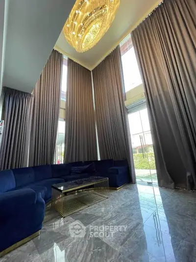 Luxurious living room with high ceilings, elegant chandelier, and floor-to-ceiling windows.