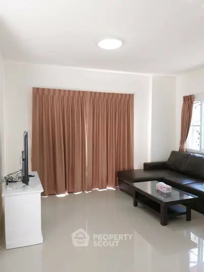 Spacious living room with sleek leather sofa and large window curtains.