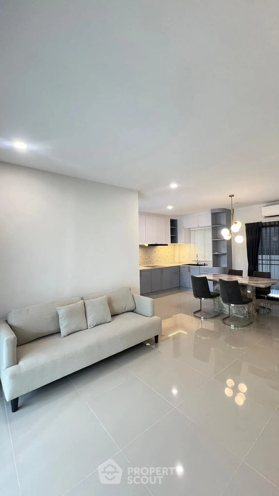 Modern open-plan living room with sleek kitchen and dining area, featuring elegant lighting and contemporary furniture.