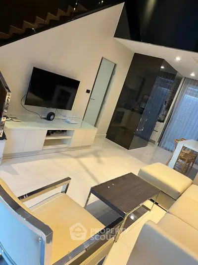 Modern living room with sleek furniture and large TV under a stylish staircase.