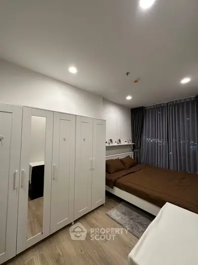 Modern bedroom with sleek white wardrobe and cozy brown bedding, featuring ambient lighting and large window view.