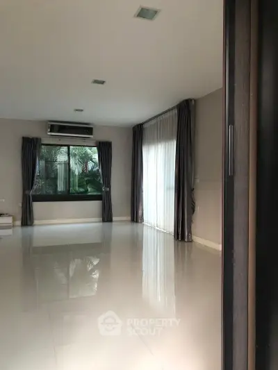 Spacious empty living room with large window and modern air conditioning unit.