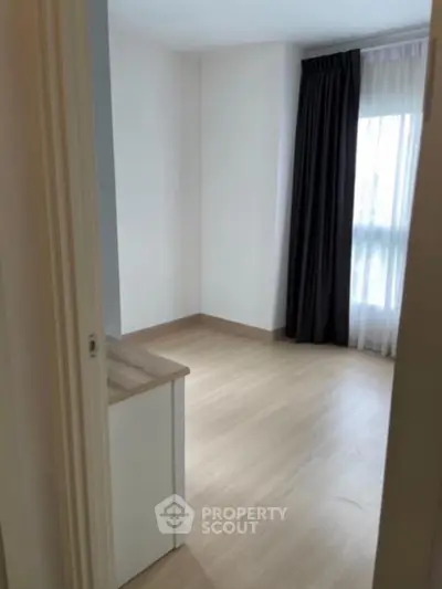 Bright empty room with wooden flooring and large window, ideal for customization.