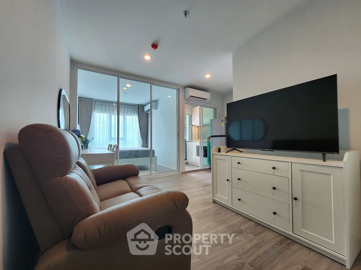 Modern living room with cozy recliner and sleek TV unit, featuring a view into a bright bedroom.