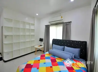 Modern bedroom with colorful bedding and built-in shelves, featuring ample natural light.