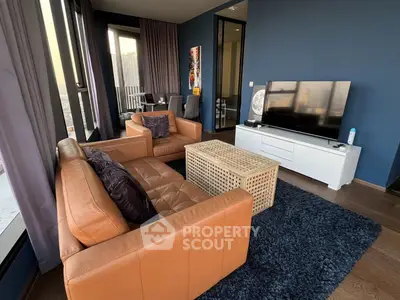 Stylish modern living room with leather sofas and large TV, featuring floor-to-ceiling windows and balcony access.