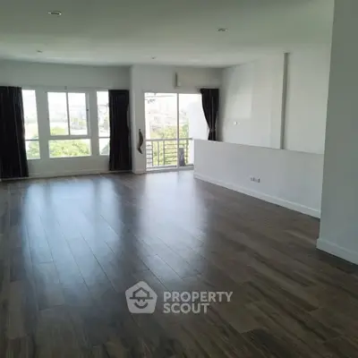 Spacious empty living room with large windows and wooden flooring, offering ample natural light and modern design.