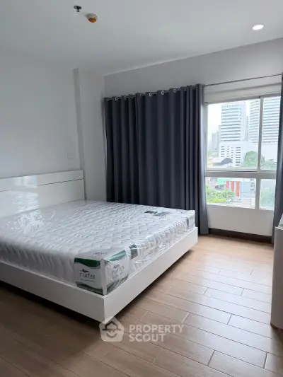 Modern bedroom with large window and city view, featuring a comfortable bed and stylish curtains.