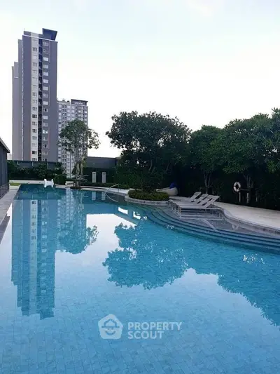 Luxurious residential pool with modern high-rise building view, surrounded by lush greenery.