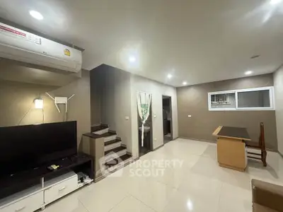 Modern living room with sleek design and staircase, featuring air conditioning and flat-screen TV.