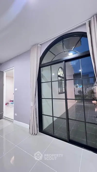 Modern interior with large arched window and elegant curtains, showcasing a stylish and spacious living area.
