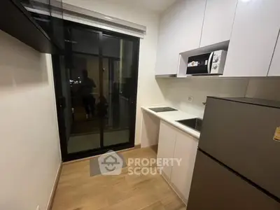 Modern compact kitchen with sleek appliances and sliding glass door to balcony