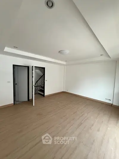 Spacious empty room with wooden flooring and modern ceiling lights, ideal for customization.