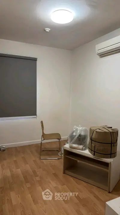 Minimalist room with wooden flooring, air conditioning, and simple furniture setup.