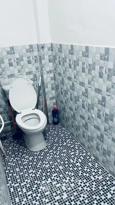 Compact bathroom with tiled walls and floor, featuring a toilet and cleaning supplies.