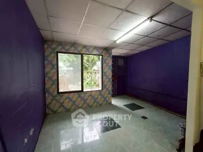 Spacious room with colorful accent wall and large window offering natural light.