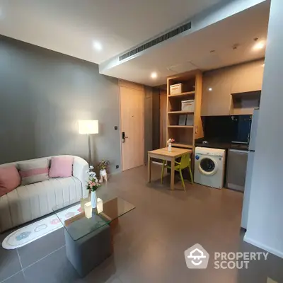 Modern living room with cozy sofa and integrated kitchen featuring washing machine and dining area.