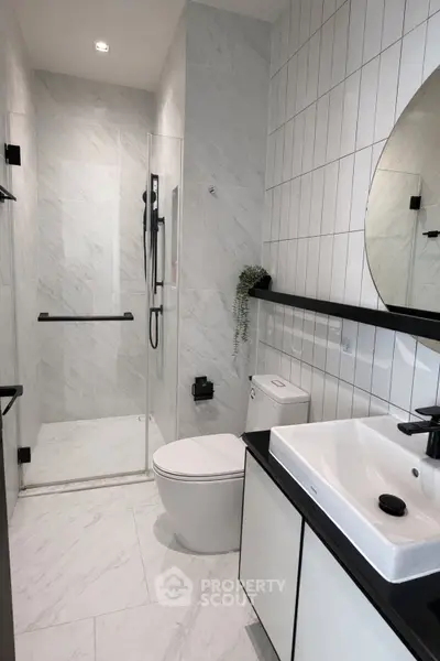 Modern bathroom with sleek design, featuring a glass shower, white tiles, and black fixtures.