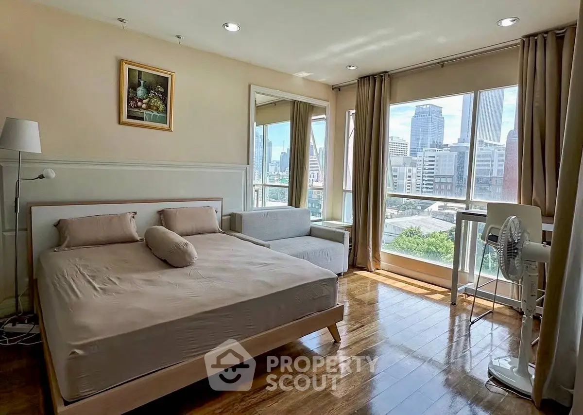 Spacious bedroom with city view, wooden flooring, and modern furnishings in a high-rise apartment.