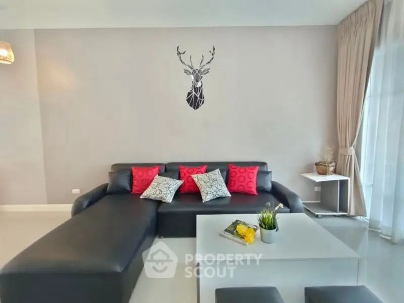 Modern living room with sleek black sofa, stylish decor, and natural light from large windows.