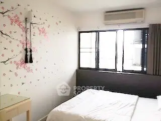 Cozy bedroom with floral wall art and large window, featuring air conditioning.