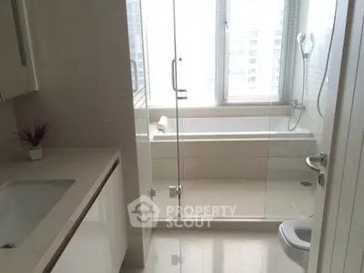 Modern bathroom with glass shower and bathtub, sleek design and natural light.