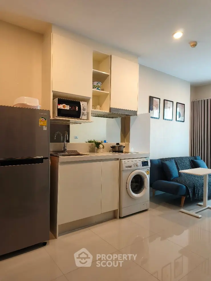 Modern compact kitchen with washing machine and cozy living area in open layout apartment.