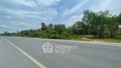 Expansive roadside land plot with lush greenery and clear skies, ideal for development opportunities.