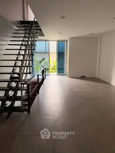 Spacious modern living room with sleek staircase and large windows for natural light.