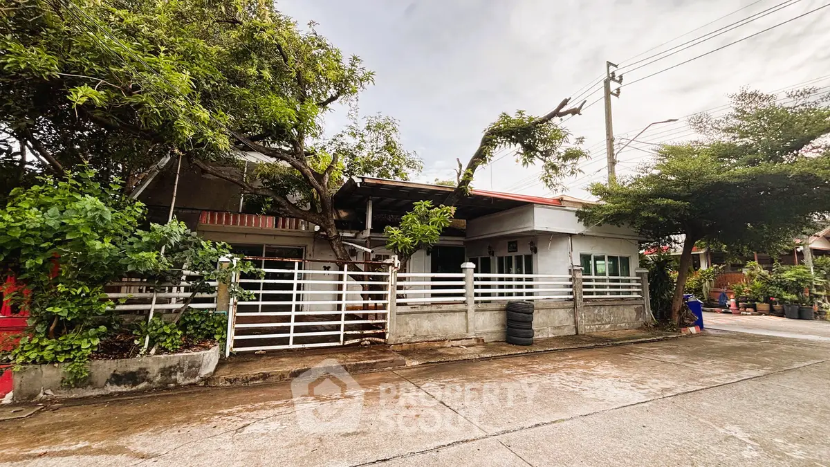Charming single-story house with lush greenery and gated entrance in a serene neighborhood.