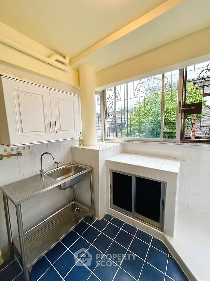 Bright kitchen with stainless steel sink and tiled surfaces, featuring large windows for natural light.