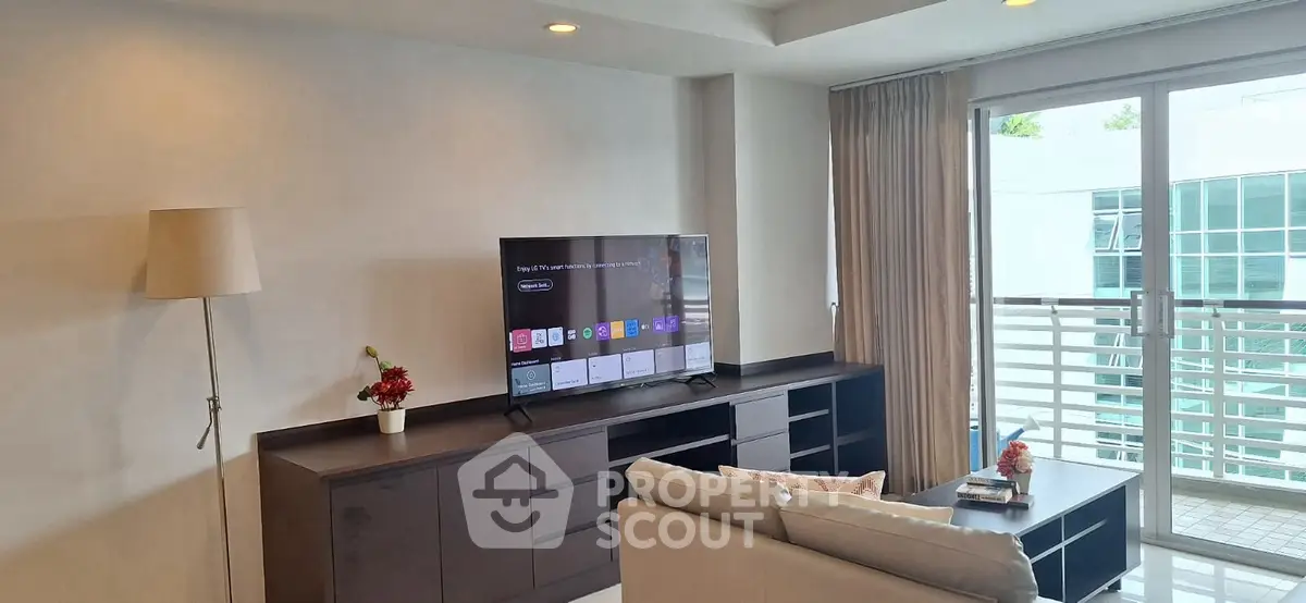 Modern living room with sleek TV setup and large windows offering natural light.