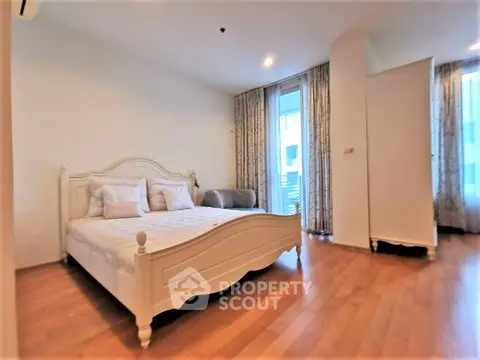 Spacious bedroom with elegant wooden flooring and stylish bed frame, featuring large windows for natural light.
