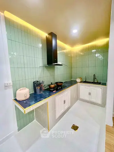 Modern kitchen with sleek design, featuring green tile backsplash and under-cabinet lighting.