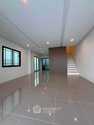 Spacious modern living room with sleek tile flooring and staircase, perfect for contemporary living.