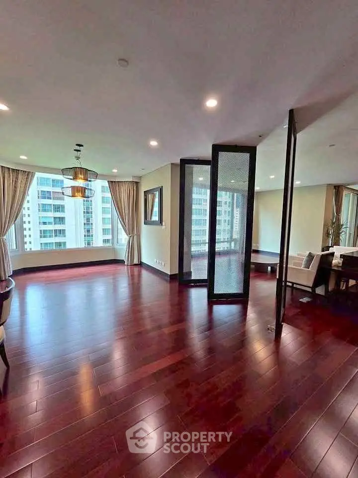 Spacious living room with hardwood floors and large windows offering city views.