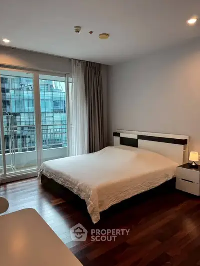 Modern bedroom with large window and wooden flooring in urban apartment