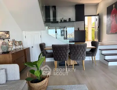 Stylish modern living room with elegant dining area and staircase, featuring plush chairs and contemporary decor.