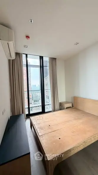 Spacious bedroom with large window offering city views, featuring minimalist wooden furniture and modern design.