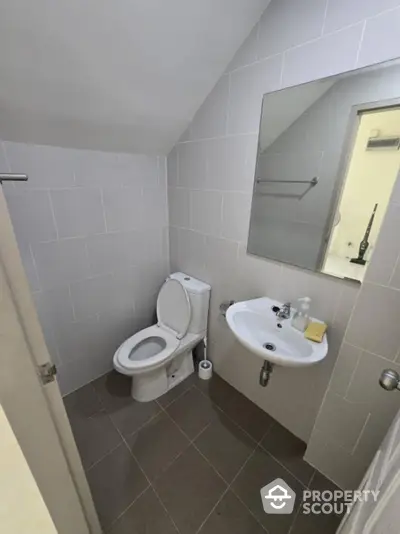 Compact modern bathroom with pristine white tiles, pedestal sink, and well-maintained toilet, ideal for urban living spaces.