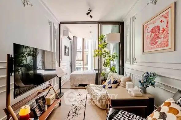 Chic living room with modern decor and large TV, leading to a cozy bedroom with natural light.
