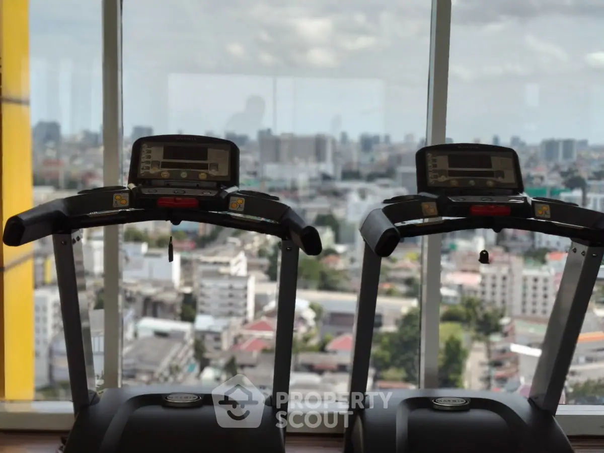 Modern gym with city view, featuring two treadmills against large windows.