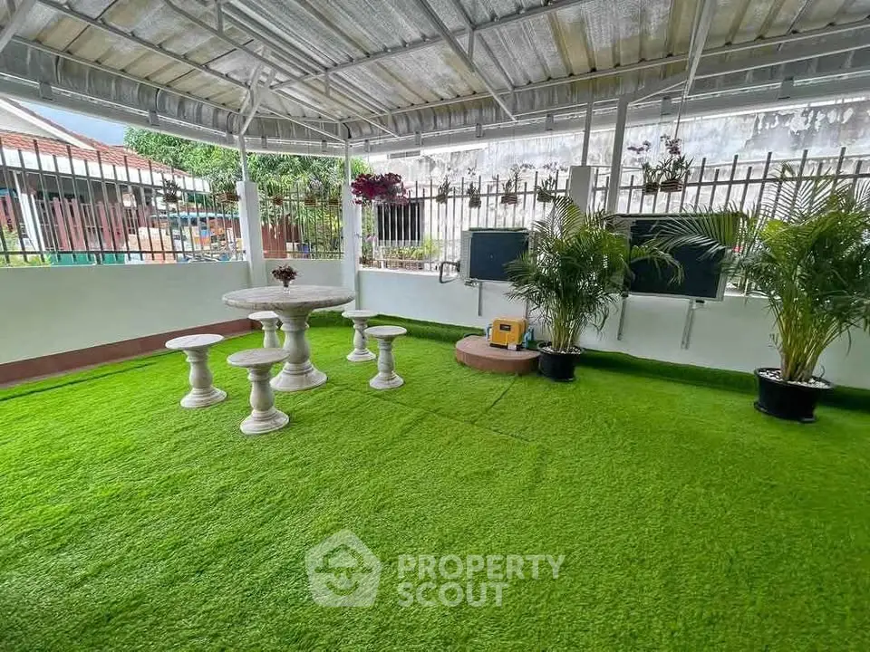 Charming garden with artificial grass and elegant stone table set under a covered patio.