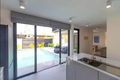 Modern kitchen with open layout and pool view, featuring sleek countertops and large sliding glass doors.