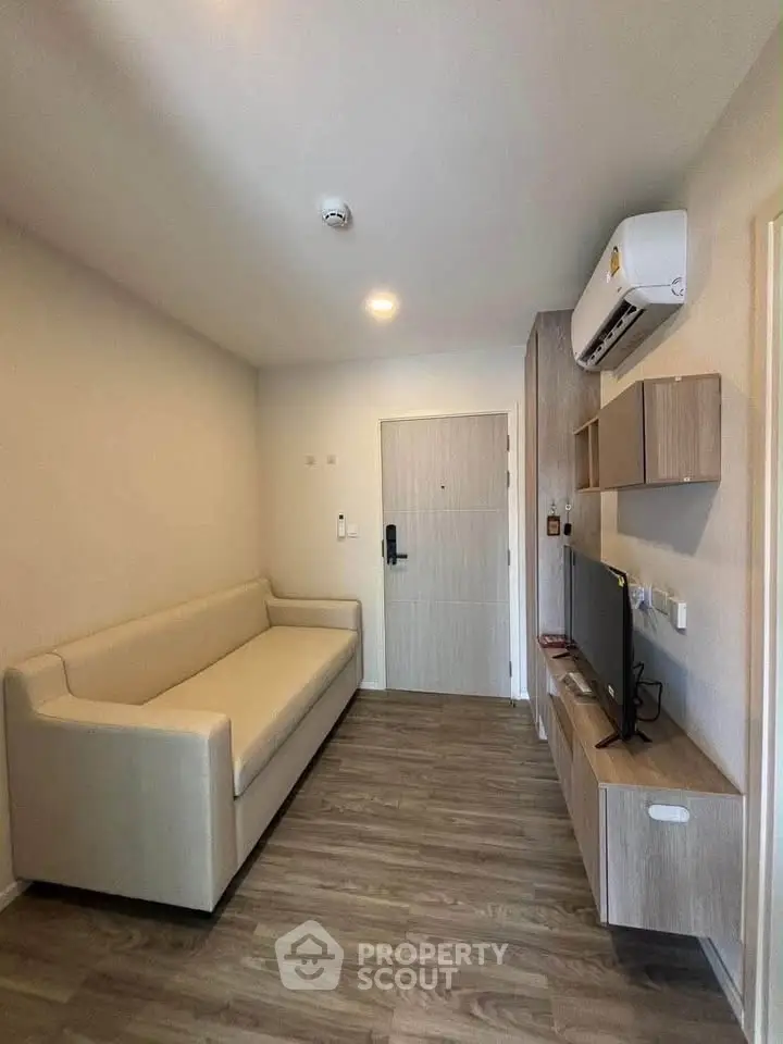 Modern living room with sleek furniture and wooden flooring, featuring a cozy sofa and wall-mounted TV.