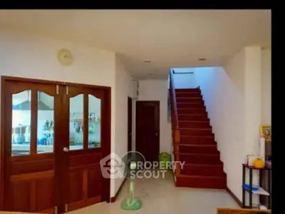 Spacious interior with wooden staircase and double doors leading to kitchen area.