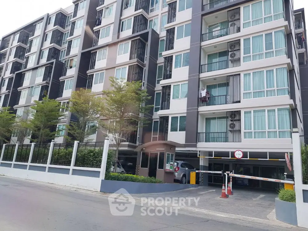Modern multi-story apartment building with gated entrance and parking area.