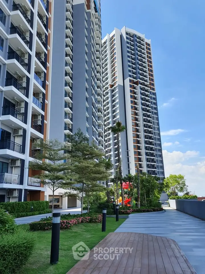 Modern high-rise residential buildings with lush landscaped garden and clear blue sky.