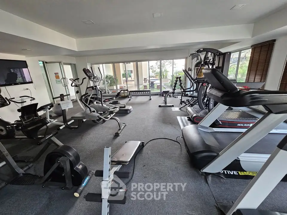 Spacious gym with modern fitness equipment and large windows for natural light.