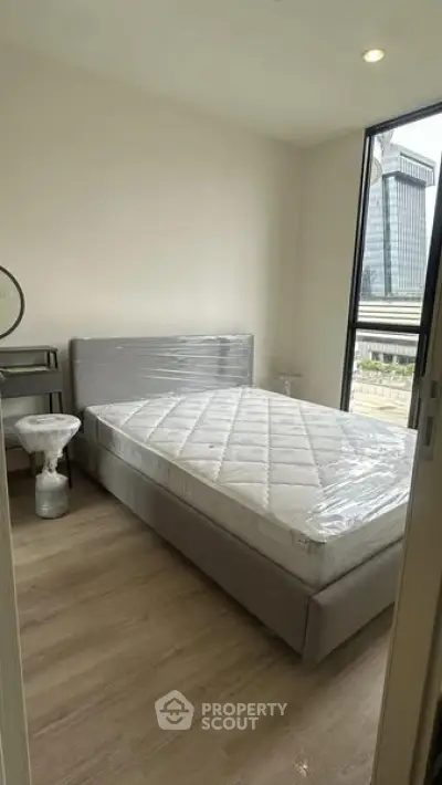 Modern bedroom with large window and city view, featuring a new bed and minimalist decor.